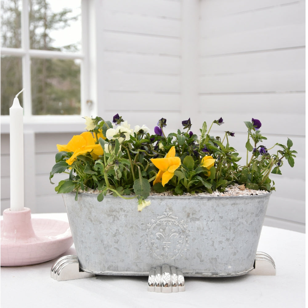 Galvanized metal planter elevated on silver POT PAWS pot feet for improved drainage and surface protection
