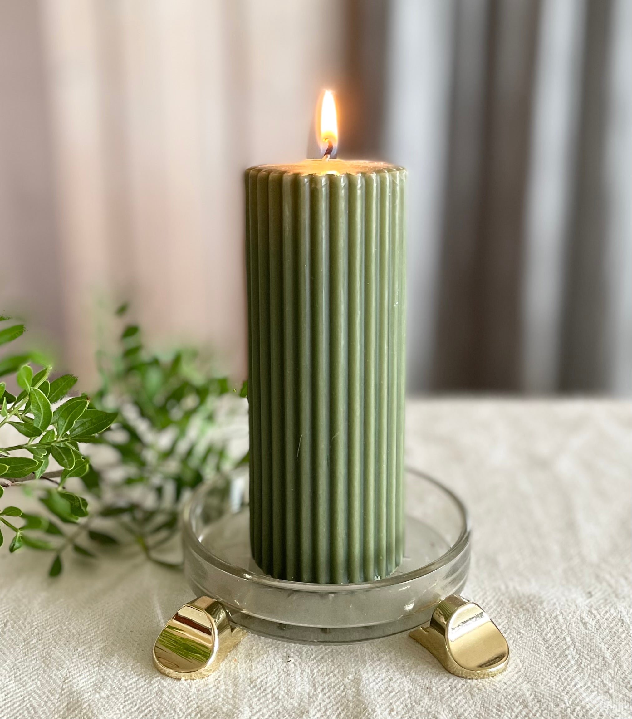 Green pillar candle displayed in a glass holder elevated with gold POT PAWS candle feet
