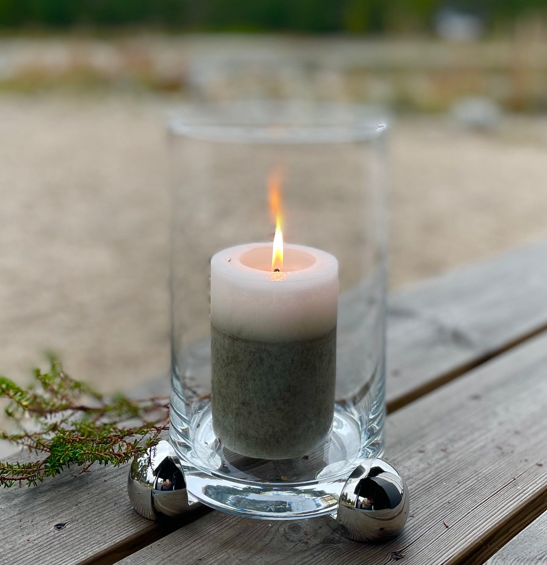 Glass candle holder with lit pillar candle elevated on silver decorative feet