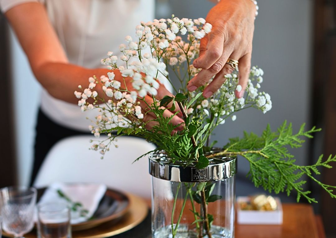 Hands arranging flowers in a glass vase with stainless steel POT PAWS rim as a table centerpiece